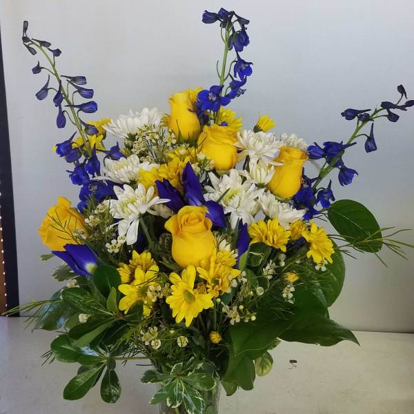 Yellow roses and white daisies in a clear glass vase with blue flowers