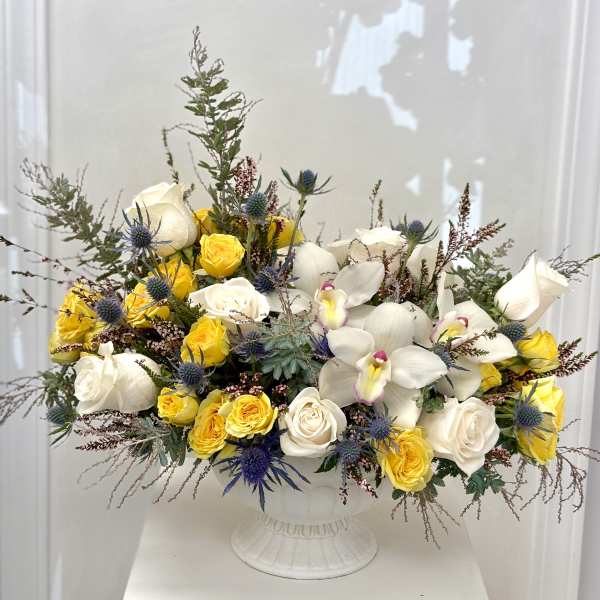 White and yellow roses with white orchids in a white pedestal vase