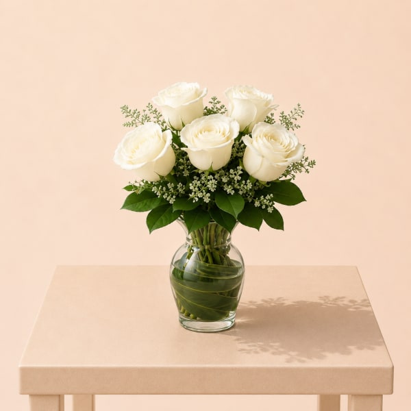 White roses arranged in a clear glass vase with greenery