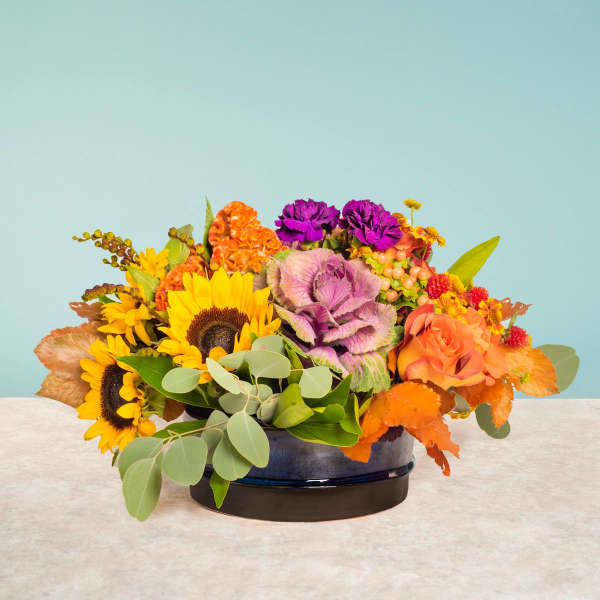 Colorful floral centerpiece with sunflowers, roses, and purple cabbage in a low vase
