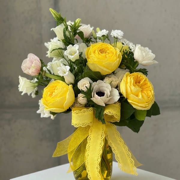 Yellow and white flower bouquet in a glass vase with a yellow ribbon