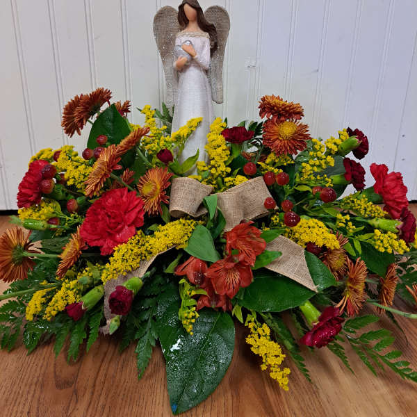 Angel figurine above a low floral arrangement with red and yellow blooms