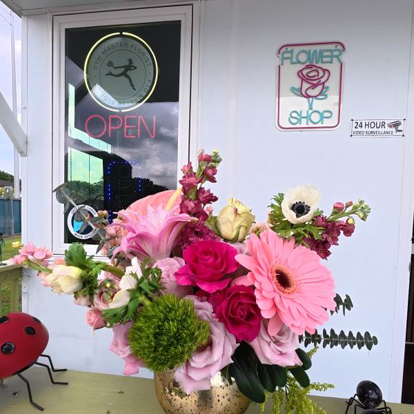 Pink and white floral arrangement in a gold vase on a porch