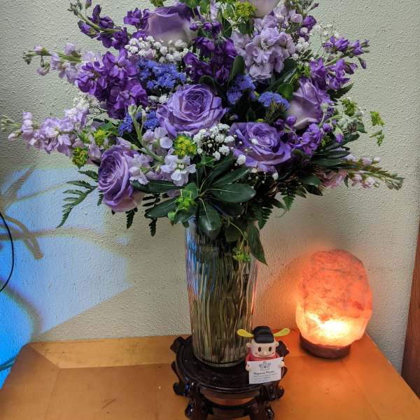 Purple floral arrangement in a glass vase on a small stand