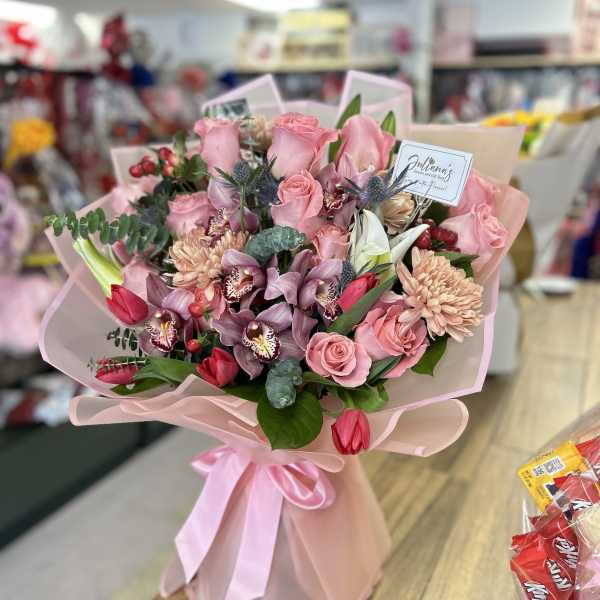 Pink rose and orchid bouquet wrapped in pale pink paper with a ribbon