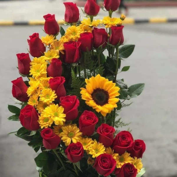 Red roses and yellow daisies arranged with a sunflower