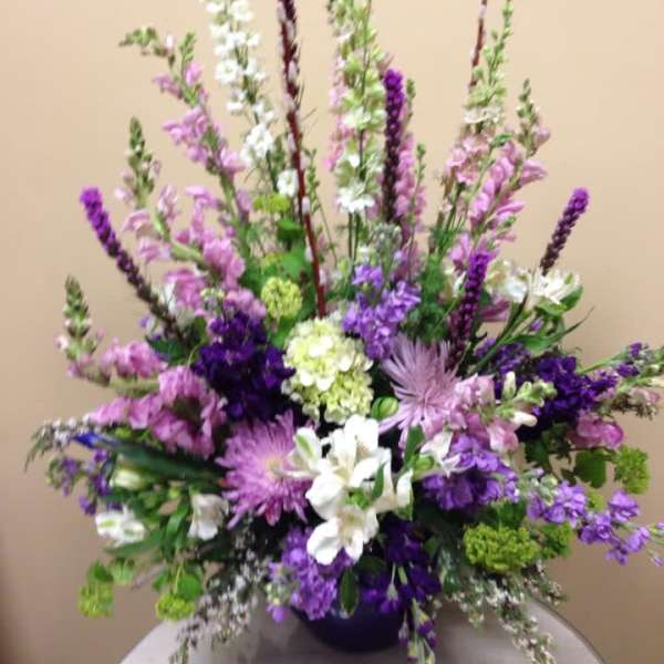 Tall purple and white floral arrangement in a dark vase