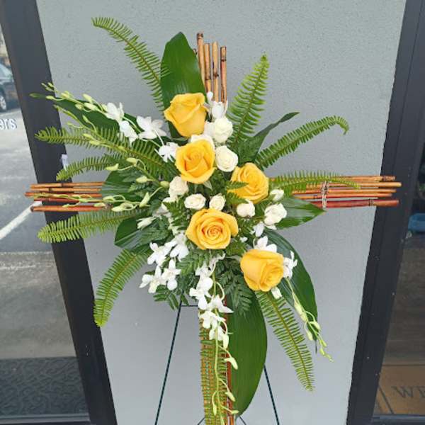 Yellow roses and white flowers arranged on a standing cross