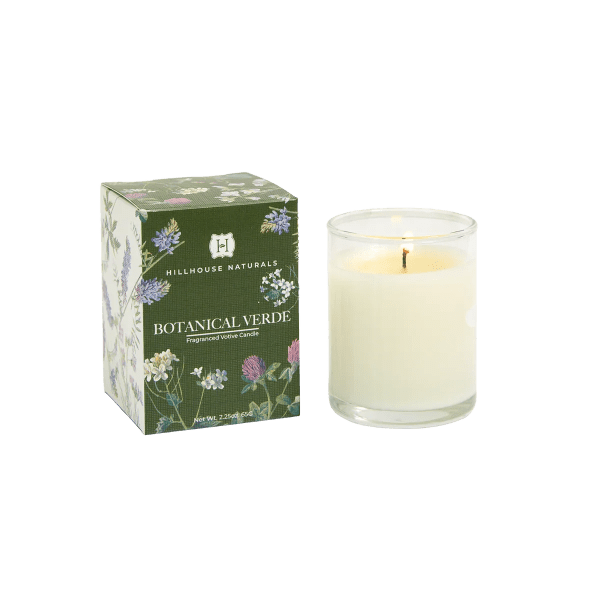 Scented white candle in a clear glass holder beside a green floral-patterned box