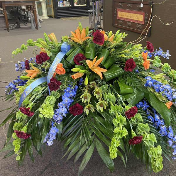 Large floral spray with orange lilies, blue flowers, and burgundy carnations