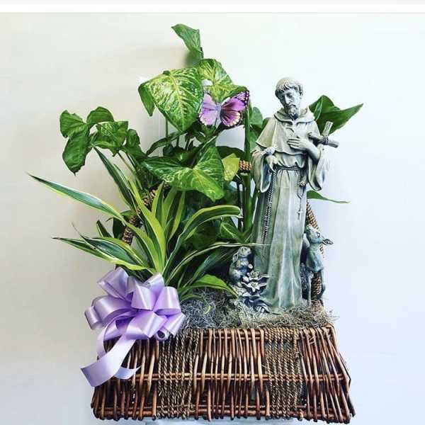 Potted plant arrangement with a saint statue and purple ribbon in a wicker basket