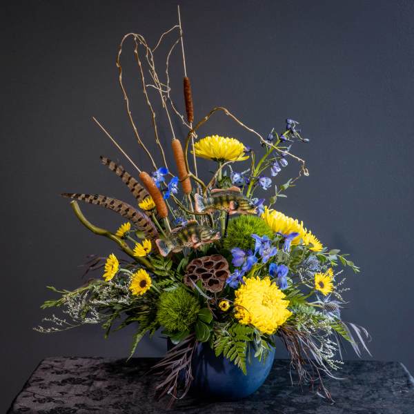 Tall floral arrangement with yellow chrysanthemums and blue flowers in a blue vase