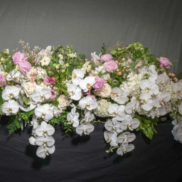 Long cascading arrangement of white orchids with pink and ivory blooms on a dark surface