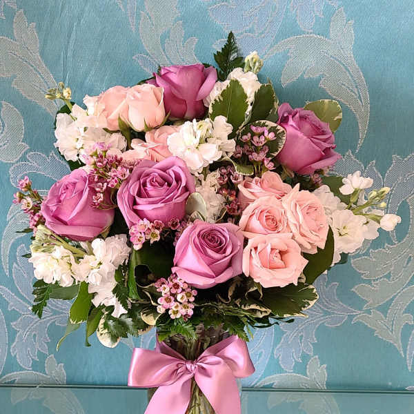 Bouquet of pink and lavender roses in a clear glass vase with a pink ribbon