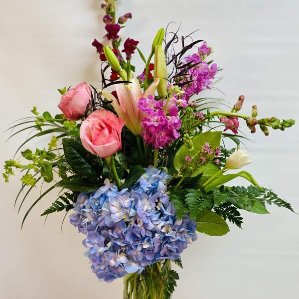 Mixed bouquet in a clear glass vase with pink roses, lilies, and blue hydrangea