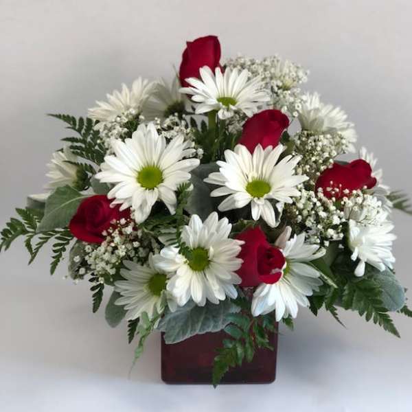 Bouquet of white daisies and red roses in a square vase