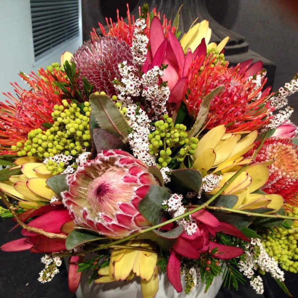 Colorful bouquet with protea, pink blooms, and yellow petals in a vase