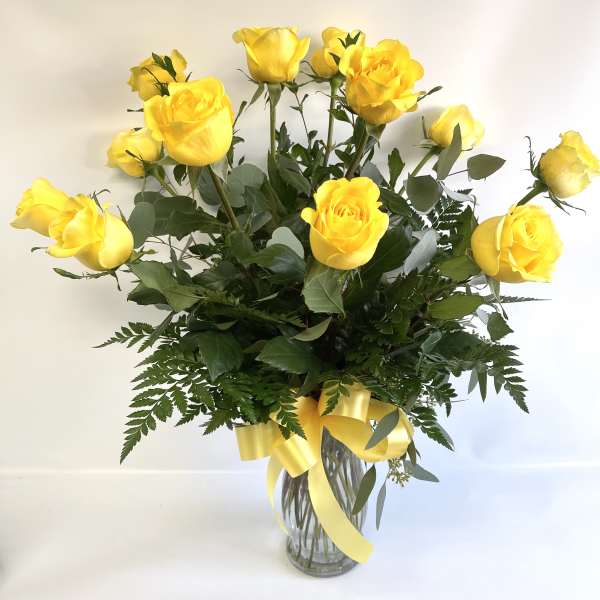 Yellow roses in a clear glass vase with a yellow ribbon