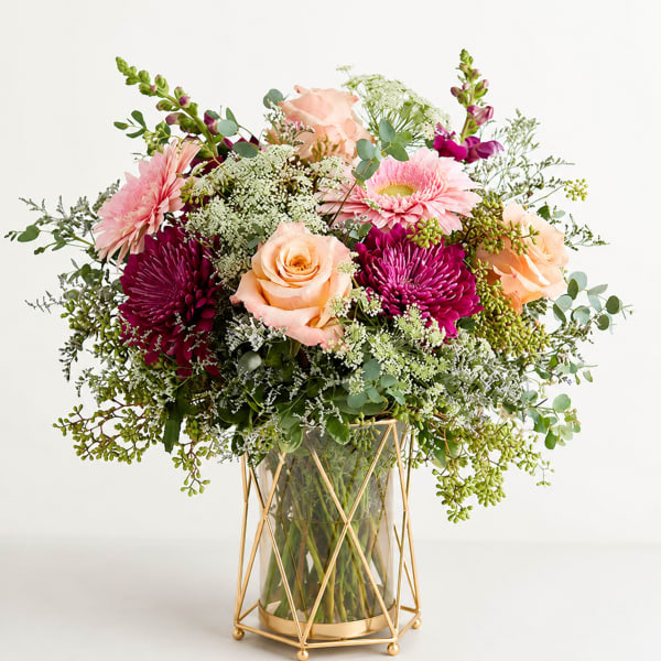Pink and peach flowers in a glass vase with a gold stand