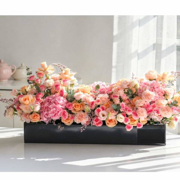 Low floral arrangement of pink and peach roses in a black rectangular container