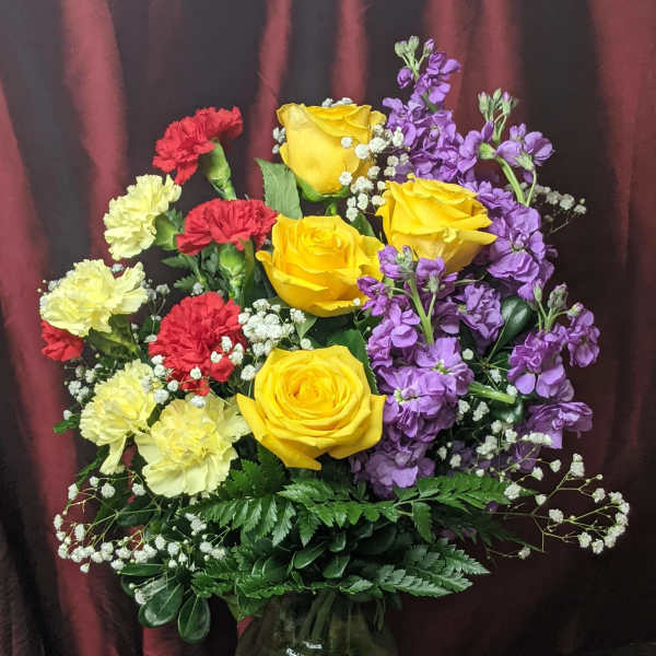 Bouquet of yellow roses, purple stock, and red and pale yellow carnations in a glass vase