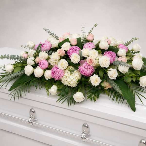 Pink and white rose casket spray with greenery on a white coffin