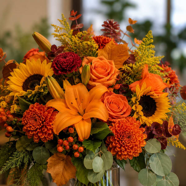 Autumn bouquet with orange lilies, roses, sunflowers, and chrysanthemums in a glass vase