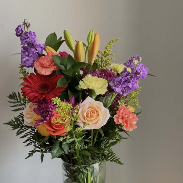 Mixed bouquet in a clear glass vase with roses, lilies, carnations, and purple blooms