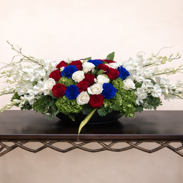 Low floral centerpiece with red, white, and blue roses and white orchids