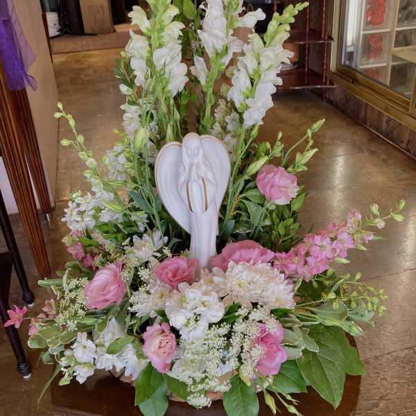 Pink and white floral arrangement with an angel figurine centerpiece