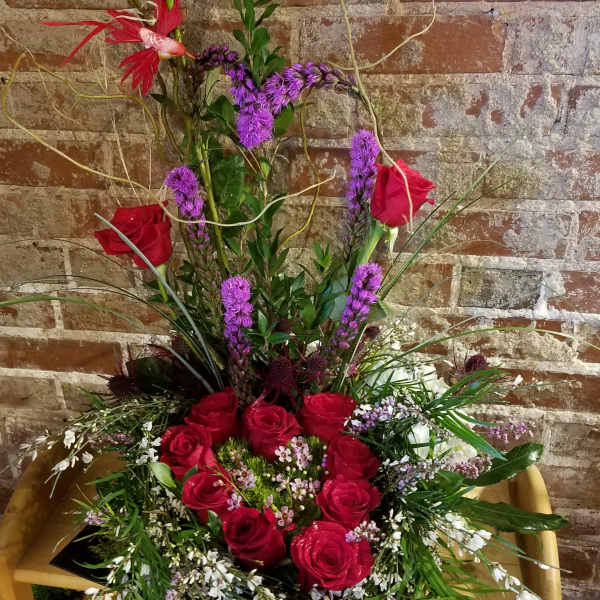 Tall arrangement of red roses and purple flowers in a wooden chair