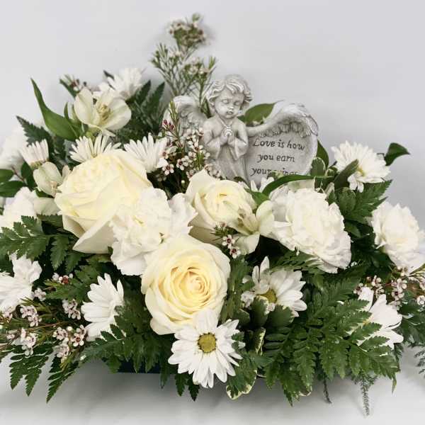 White floral arrangement with roses and daisies around an angel figurine