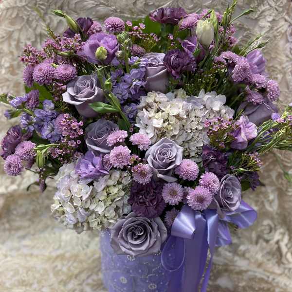 Lavender and purple bouquet with roses, hydrangeas, and ribbon in a purple vase