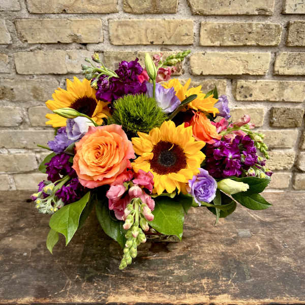 Mixed bouquet with sunflowers, roses, and purple blooms in a low arrangement