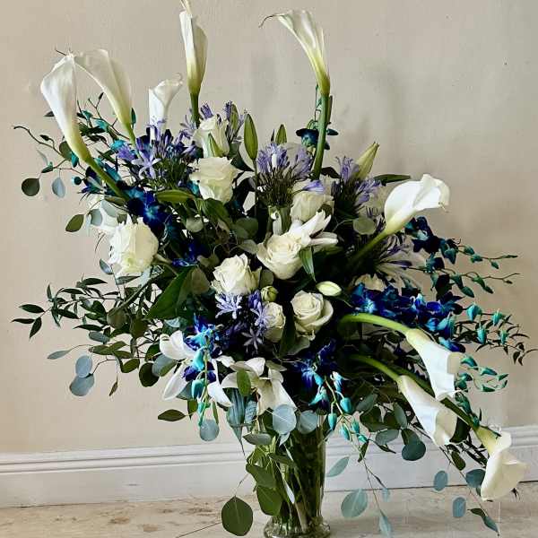 Tall bouquet of white calla lilies, roses, and blue flowers in a glass vase