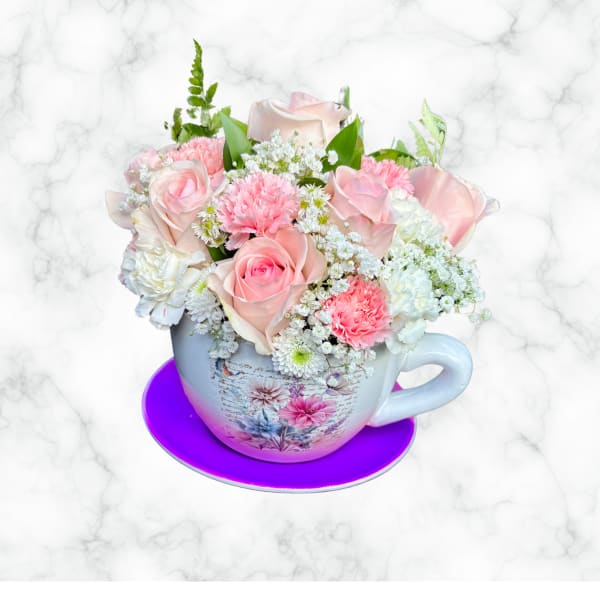 Pink and white flower arrangement in a teacup with saucer