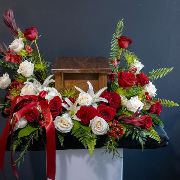 Red and white roses arranged around a wooden urn with a red ribbon