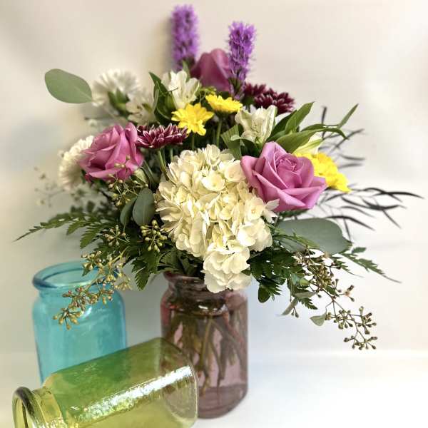 Mixed bouquet in colorful glass jars with pink roses and white hydrangea
