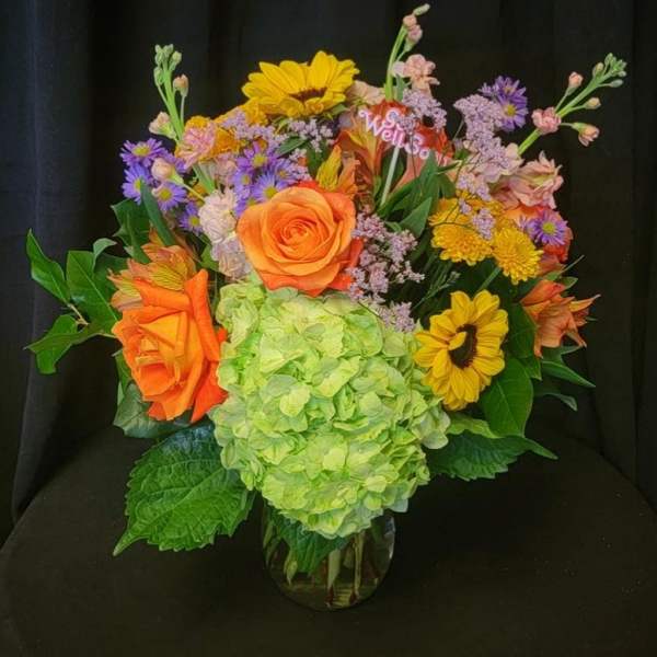 Colorful mixed bouquet with hydrangea, roses, and sunflowers in a glass vase
