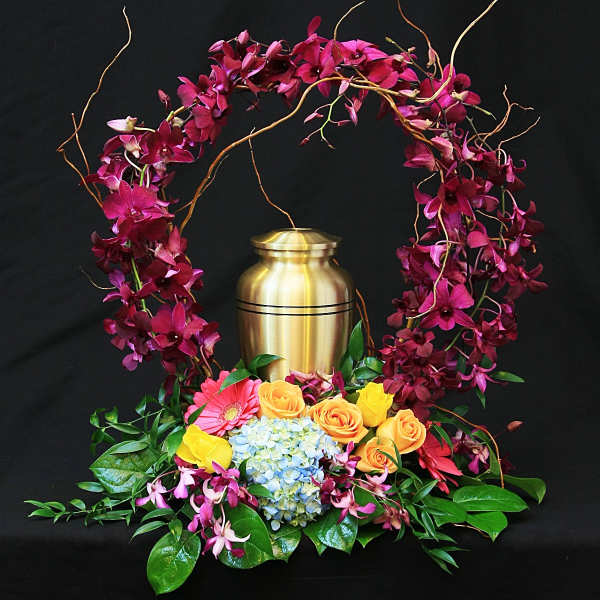 Floral urn arrangement with magenta orchids, roses, and hydrangea around a gold urn
