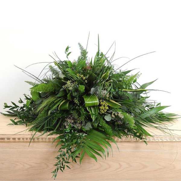 Large low arrangement of assorted green foliage on a wooden casket