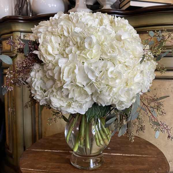 White hydrangea bouquet in a clear glass vase with eucalyptus accents