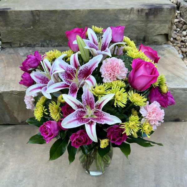 Bouquet of pink roses, lilies, and yellow mums in a glass vase