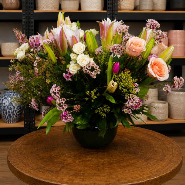 Mixed bouquet of lilies, roses, and small pink blossoms in a black vase