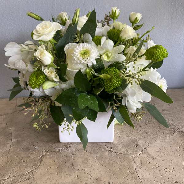 White floral arrangement in a square vase with green accents