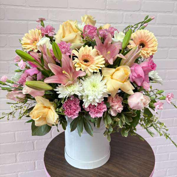 Mixed bouquet of pink and yellow flowers in a white hatbox