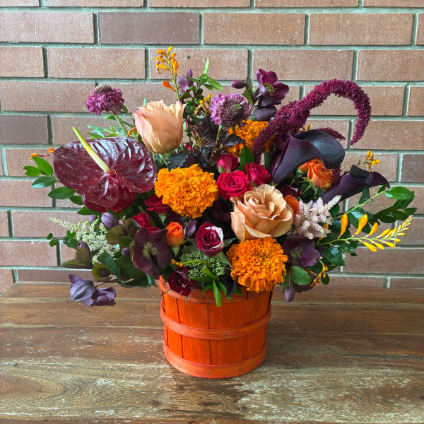 Mixed bouquet in an orange basket with roses, calla lilies, and marigolds