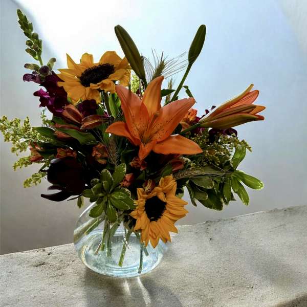 Bouquet of orange lilies and sunflowers in a clear glass vase