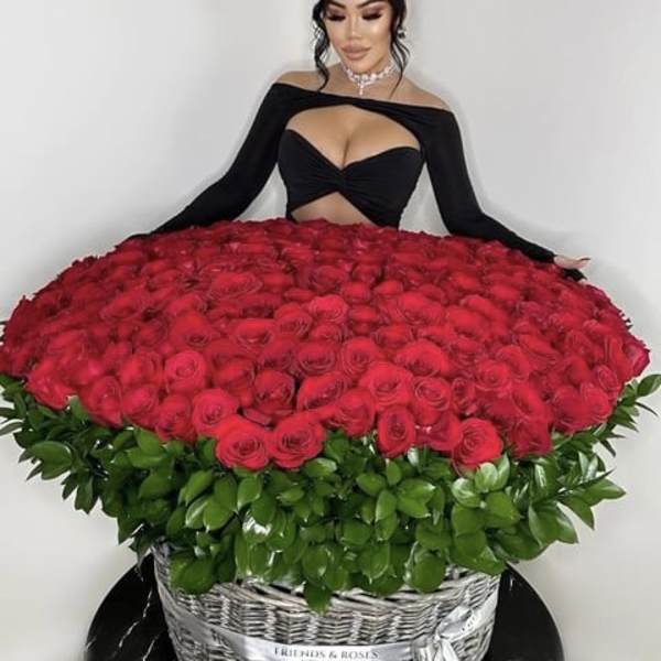 Large basket of red roses with green foliage and a woman in black behind it