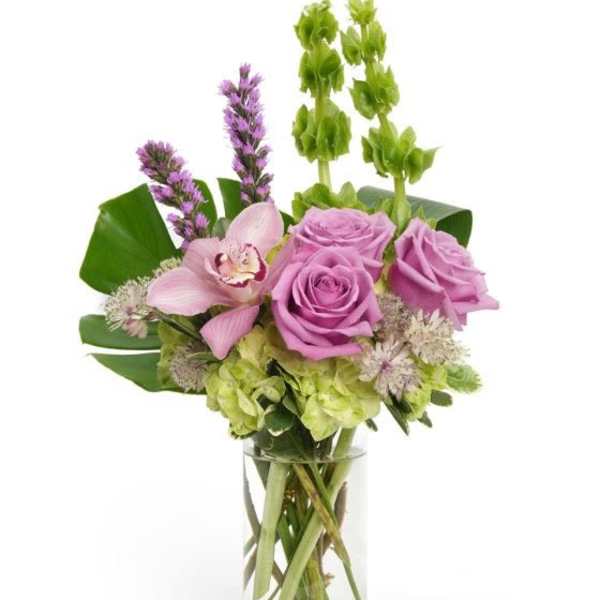 Tall arrangement of lavender roses, green hydrangea, Bells of Ireland and a pink orchid in a clear glass vase